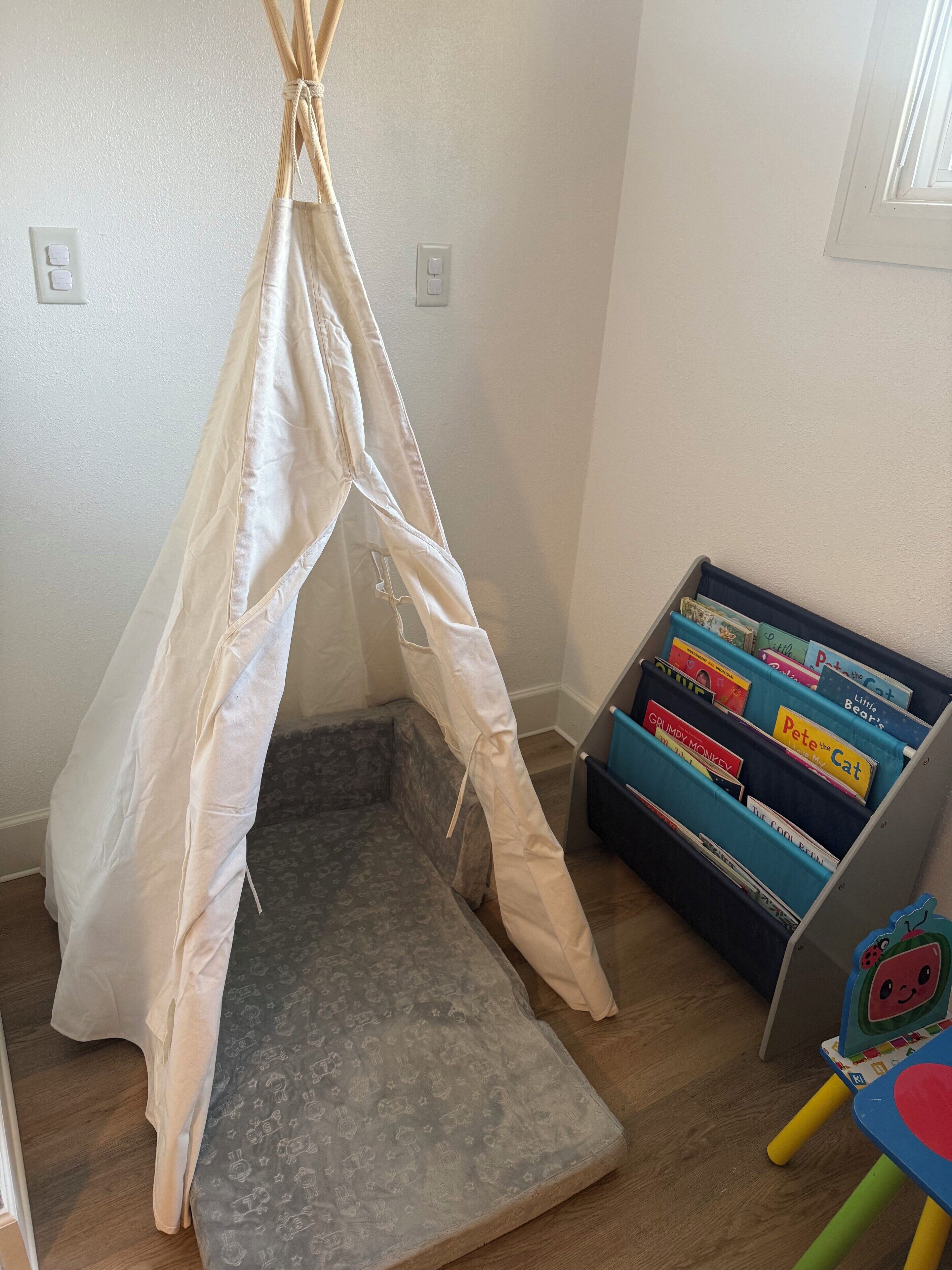 Una habitació amb una estructura semblant a una tenda, una estanteria plena de llibres infantils i un matalàs estampat al terra.