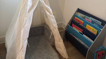 A room with a tent-like structure, a bookshelf with children's books, and a patterned mattress on the floor.