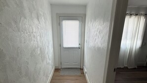 Un pasillo con paredes de diseño, suelo de madera, una puerta con ventanal y vistas a una habitación con cortinas.