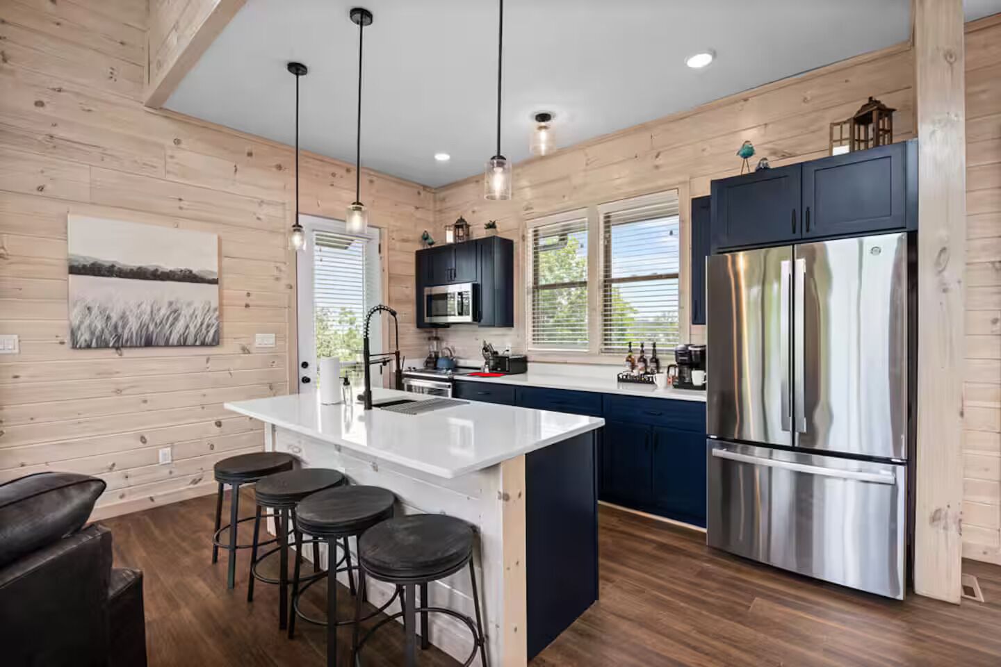A modern kitchen with a central island, bar stools, stainless steel appliances, and wooden paneling.