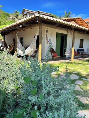 Une maison avec une véranda, des hamacs et un jardin.