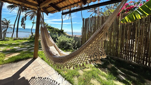 Un hamac sous une pergola en bois, une terrasse carrelée et une vue sur la mer.