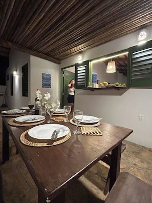 A dining table set with plates, cutlery, and glasses, a hanging light fixture, and a window with shutters. - Relax with incredible views, 80 meters from the sea, pet-friendly. (Icapuí)