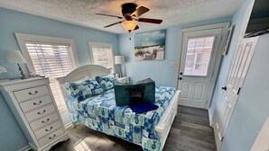 Un dormitorio con cama, cómoda, ventilador de techo y ventanas.