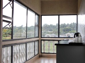 A room with large windows, a balcony with balustrades, and a kitchen area with a coffee maker.