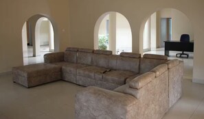 A spacious living room with a large sectional sofa, a desk with a chair, and arched doorways leading to other areas.