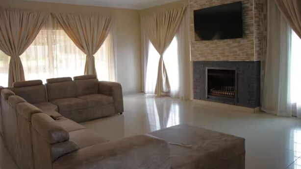 Uma sala de estar espaçosa com um amplo sofá modular, uma TV de tela plana fixada em uma parede de pedra e uma lareira.