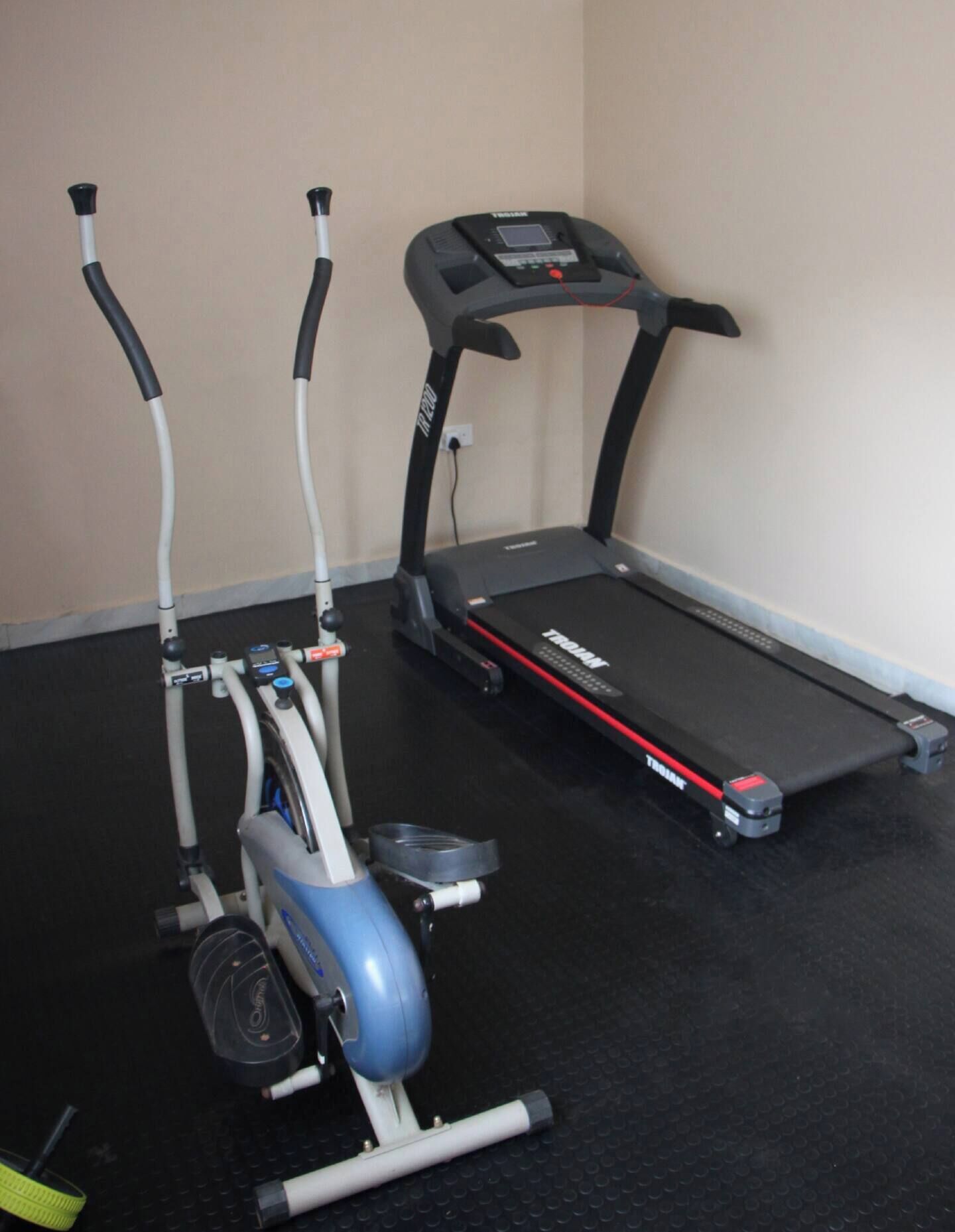 A treadmill and an elliptical machine in a room with a black floor and beige walls.