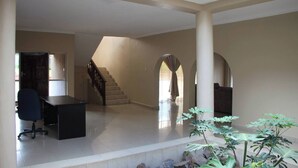 Um interior espaçoso com escadas, uma escrivaninha e uma cadeira, além de uma grande planta em primeiro plano.