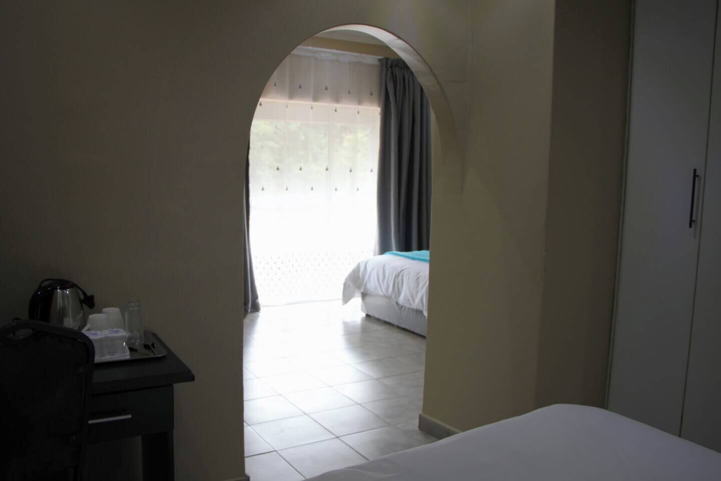 A hotel room with a bed, a desk with a kettle, and a wardrobe.