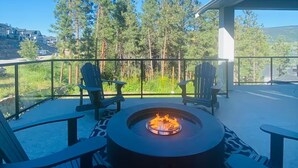 A fire pit with chairs on a balcony overlooking a forested area.