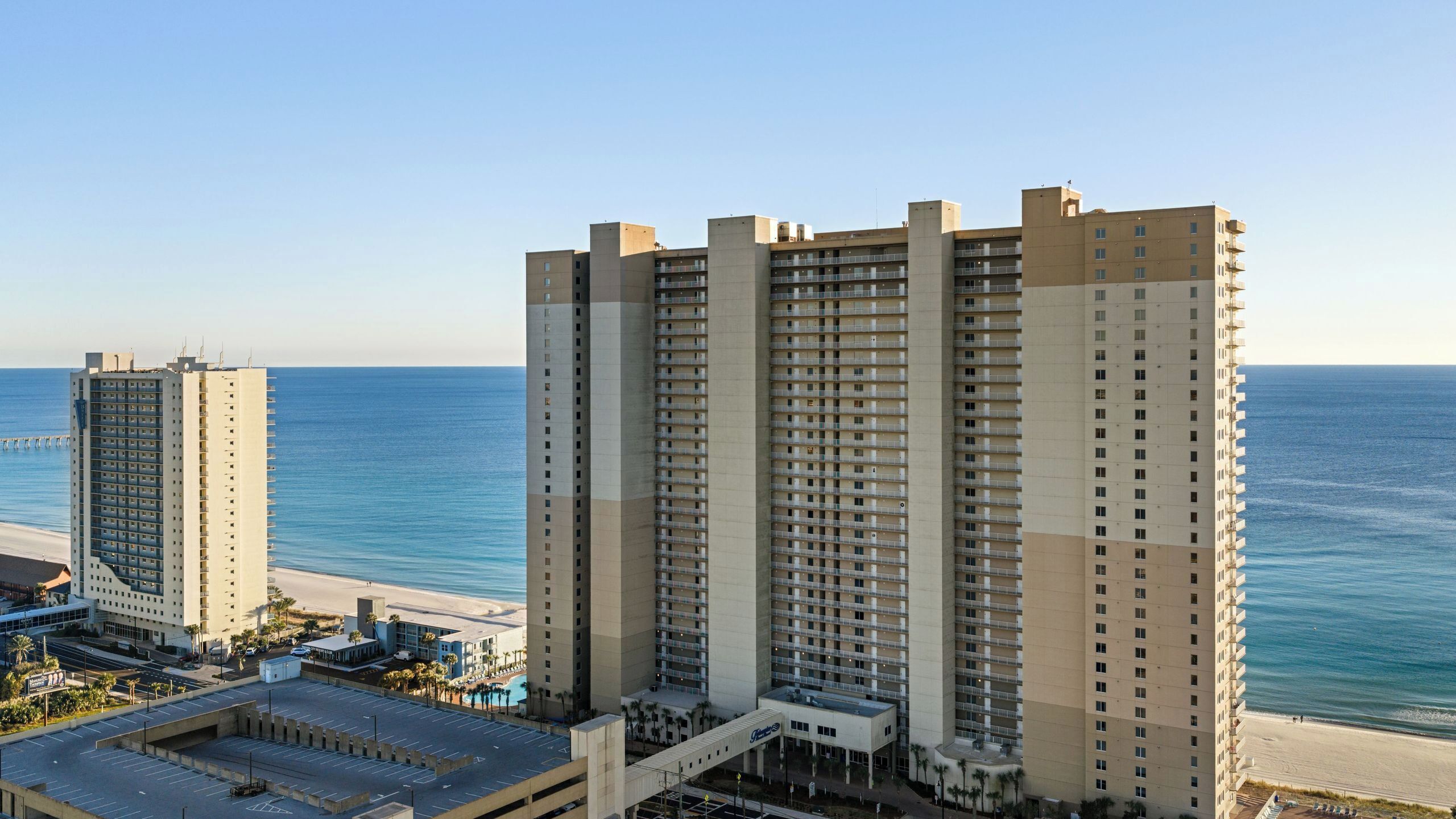 Um hotel moderno com vários andares, vista para a praia e área de estacionamento.