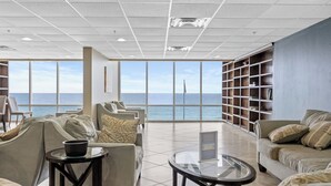 Amplia sala de estar con vista al océano, con asientos cómodos, una mesa de centro de vidrio y una estantería.