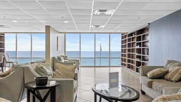 Amplia sala de estar con vista al océano, con asientos cómodos, una mesa de centro de vidrio y una estantería.