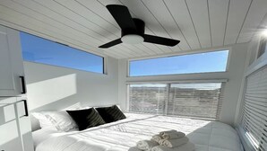 Una camera da letto con un letto grande, biancheria da letto bianca, una ventola a soffitto e vista sul cielo attraverso le finestre.