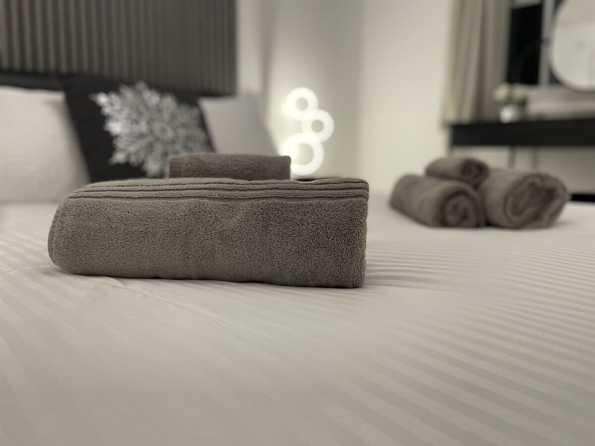 A neatly made bed with a folded gray towel and a rolled towel in the background.