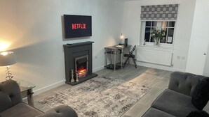 A living room with a fireplace, a TV mounted above it, a sofa, and a window with blinds. - Modern 3 Bedroom high spec house in Sheffield (Handsworth)