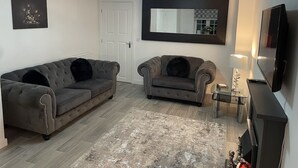A living room with two grey sofas, a large mirror, a flat-screen TV, and a small table with a lamp. - Modern 3 Bedroom high spec house in Sheffield (Handsworth)