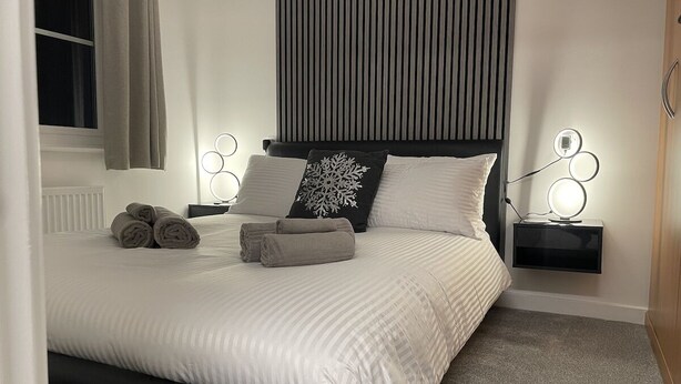 A neatly made bed with rolled towels, a black headboard, and bedside lamps. - Modern 3 Bedroom high spec house in Sheffield (Handsworth)