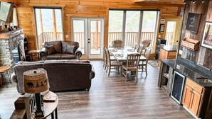 Ein gemütliches Blockhaus-Interieur mit Kamin aus Stein, einer Couch, einem Esstisch mit Stühlen und einer Küchenzeile.