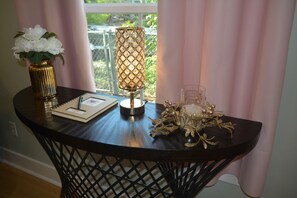 Una mesa de madera oscura con una lámpara decorativa, un jarrón con flores blancas, un vaso y un cuaderno.