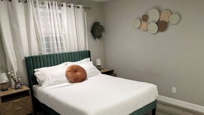 Un lit bien fait, avec du linge de lit blanc et une tête de lit verte, une table de chevet avec une lampe et un élément décoratif mural.