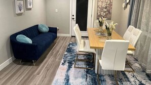 Une pièce moderne avec un canapé bleu foncé, une table à manger en bois et des chaises blanches, ainsi qu’un tapis bleu à motifs.