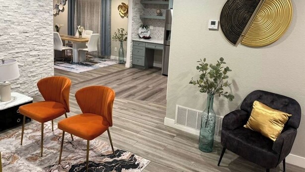 Un salon moderne avec un mur en pierre, un coin repas avec une table et des chaises, et une cuisine en arrière-plan.