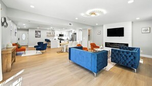 Ein modernes Wohnzimmer mit Kamin, blauen Sofas und einer Küche im Hintergrund.
