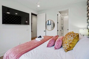 Una camera da letto con un letto grande, una coperta rosa e un cuscino dorato. Si vede uno specchio a parete e una finestra con vista.