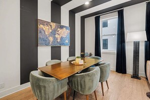 Zona pranzo con tavolo in legno, sedie rivestite di grigio, un'opera d'arte raffigurante una mappa del mondo e una finestra con tende.