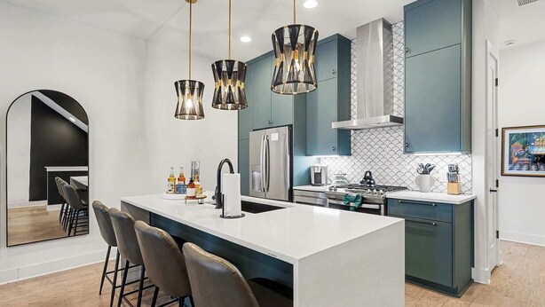 Cozinha moderna com ilha central, banquetas, iluminação pendente e geladeira de aço inoxidável.