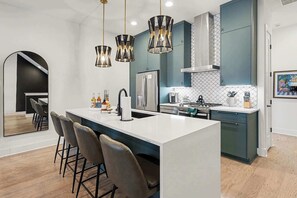 Una cocina moderna con una isla central, taburetes de bar, iluminación colgante y un refrigerador de acero inoxidable.