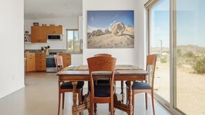 A modern kitchen with wooden cabinets and a dining area with a large window overlooking a desert landscape. - Juniper House - Desert Retreat near JTNP - Stargazing, Views & Spa (Joshua Tree)