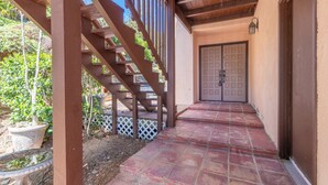 A covered outdoor area with a wooden staircase leading to a door. - Casa De La Campanita
1 Bed, 1 Bath (San Marcos)