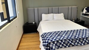 Et hotelværelse med en stor seng, et natbord, et skab og et fjernsyn på væggen samt en hylde med genstande.