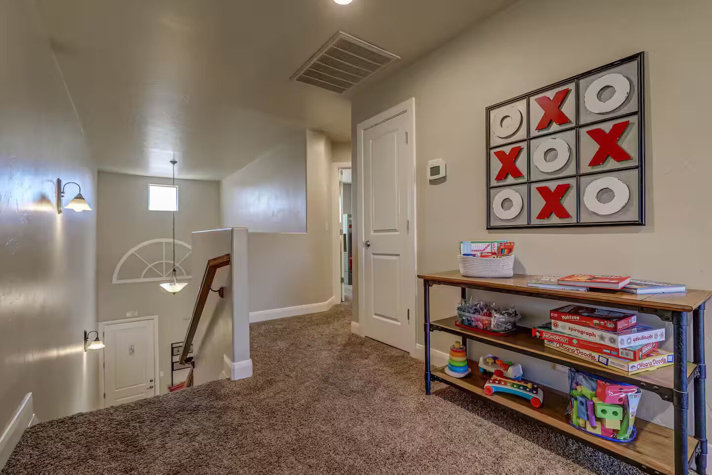 A hallway with carpeted flooring, a door, a wall-mounted game board, and a shelf with board games.