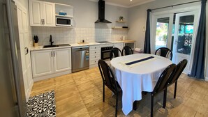 A compact kitchen with white cabinets, a microwave, a stove, and a sink. There's a dining table with chairs and a ceiling fan. - Central 1940s Bendigo Home Hamptons Heritage Reno (Long Gully)