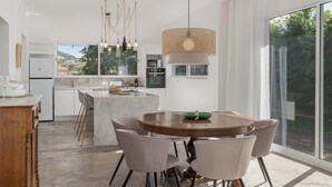 Una cocina moderna con una isla grande, armarios blancos y un comedor con mesa y sillas de madera redonda.