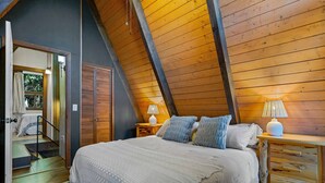 Ein Schlafzimmer mit schräg verlaufender Decke, einem Bett mit weißer Bettdecke, zwei Nachttischen mit Lampen und einem Holzbeistelltisch.