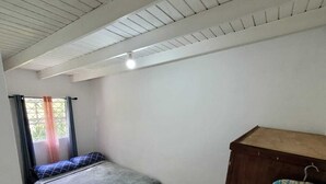 Una habitación pequeña y limpia con una cama individual, un armario de madera y una ventana con cortinas.