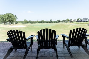 Three black Adirondack chairs on a brick patio overlooking a golf course.