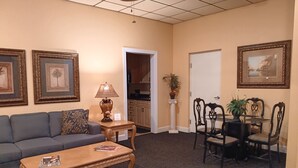 A hotel room with a sofa, a wooden coffee table, a dining table with chairs, a lamp, framed pictures on the walls, and a potted plant. - Villa C-Villa Ensuite (Gulfshores)