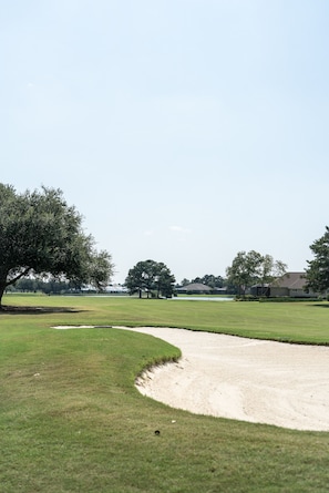 Un campo de golf con búnkeres de arena, árboles y casas al fondo.