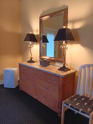 A room with a wooden dresser, two lamps, a mirror, a chair, and a white appliance.