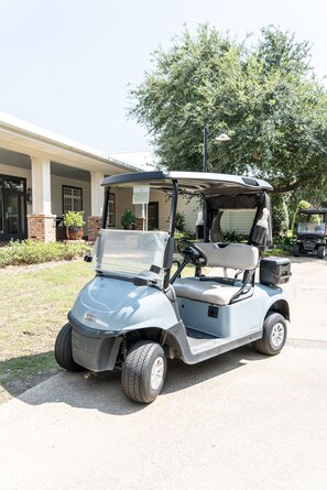 A golf cart parked in front of a building with a covered porch and potted plants.