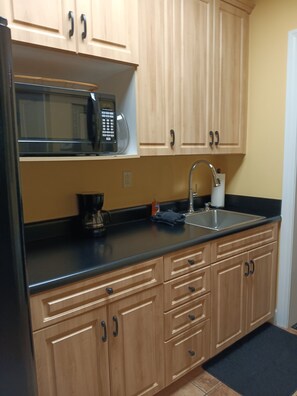 Una cocina con armarios de madera, microondas, pileta y cafetera.