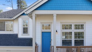 Una casa de dos pisos con puerta azul, revestimiento blanco y un porche de madera con sillas.