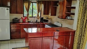 A kitchen with wooden cabinets, a refrigerator, a microwave, a stove, and a sink. - Casa Mango Two-bedroom home a short 4-minutes walk from the ocean, w/ pool & BBQ (Guanacaste Province)