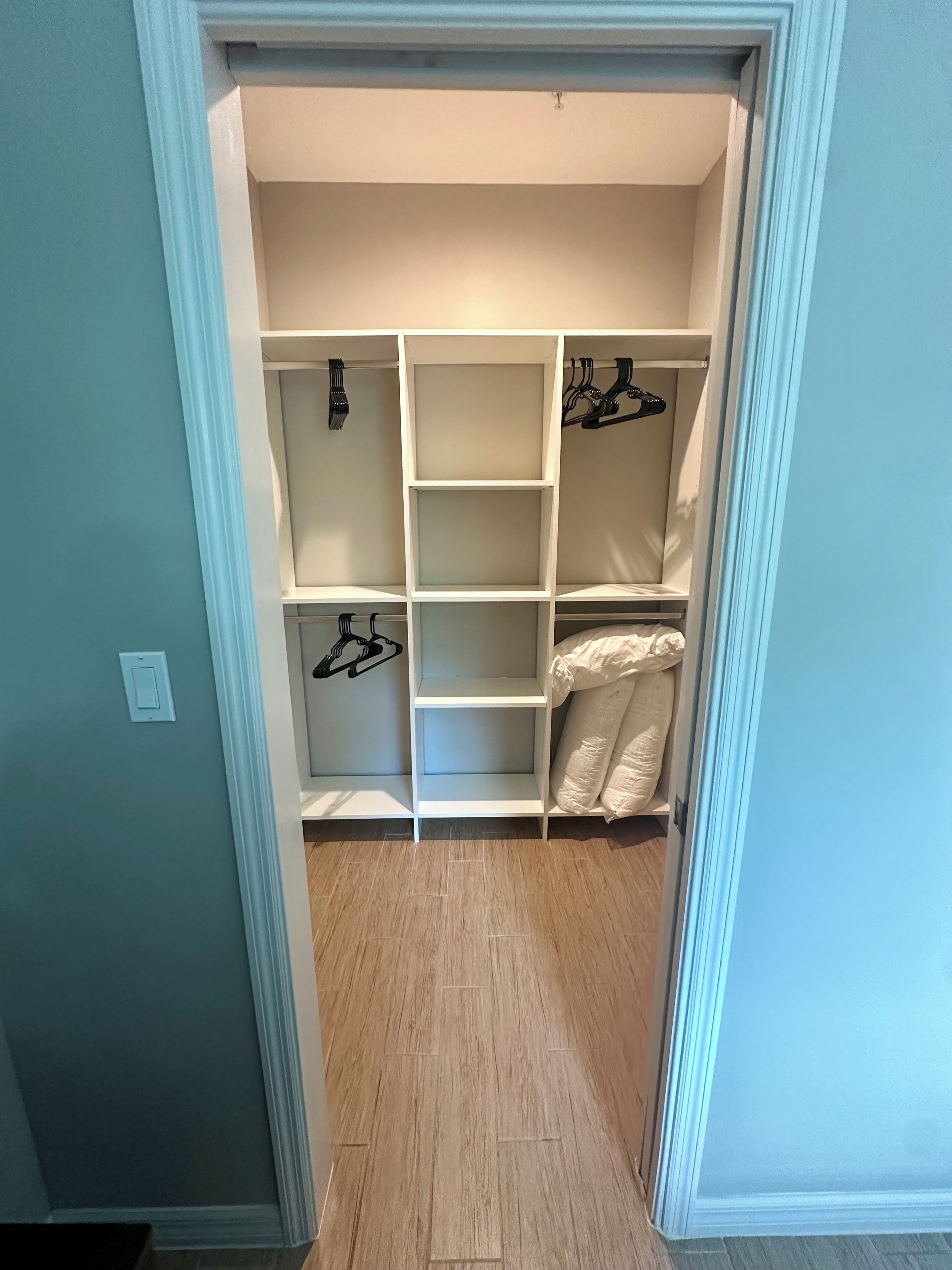 A walk-in closet with multiple shelves and hanging space, light-colored walls, and a wooden floor.